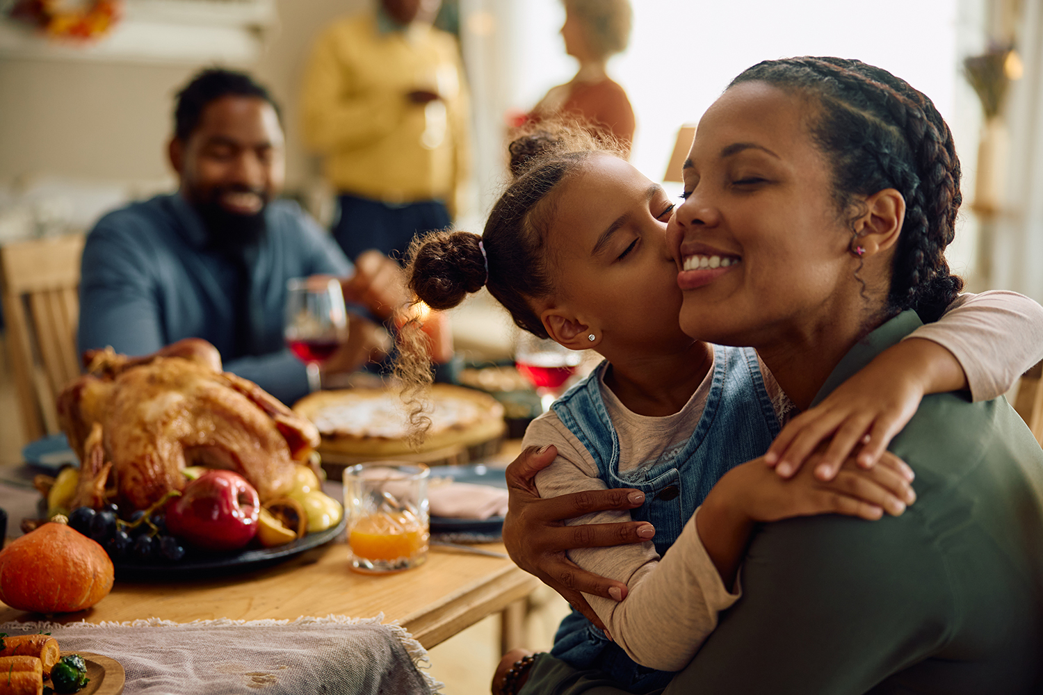Grateful black girl kisses her mother during Thanksgiving family meal.